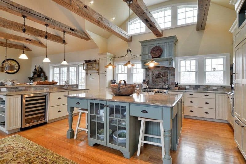 blue kitchen island with textured glass faced base and antique white cabinetry with custom range hood matching island and starfish decoration on windows