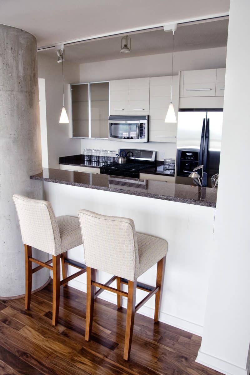 budget friendly short backsplash and concrete column with granite bar countertop and track pendant lights and modular cabinets with frosted glass cabinet doors