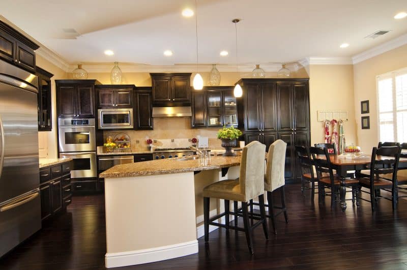 dark accent tiles on backsplash and decorative clear glass jugs with curved kitchen island and teardrop pendant lights and dark stain on hardwood floor