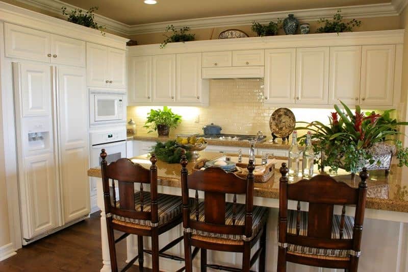 ecru glossy subway tile backsplash and wooden high back barstools with crown molding and single waterfall edge granite counter edge and raised center panel cabinetry
