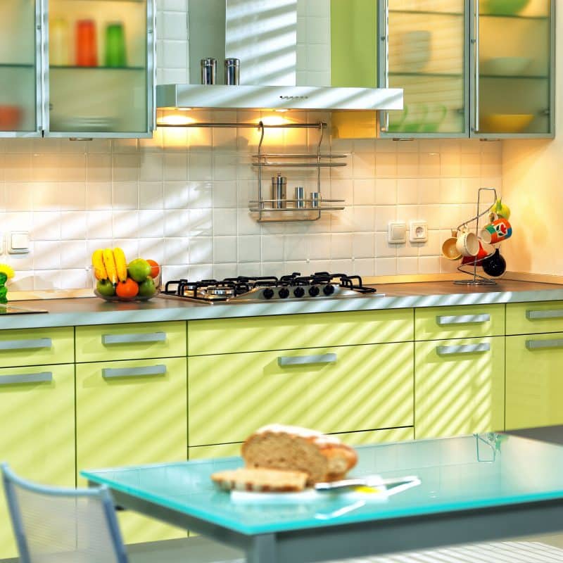 lower cabinets in yellow lime tones and brushed stainless steel cabinet handles with frosted glazed center panel upper cabinet and lighting inside cabinets and range hood with flat top for additional storage