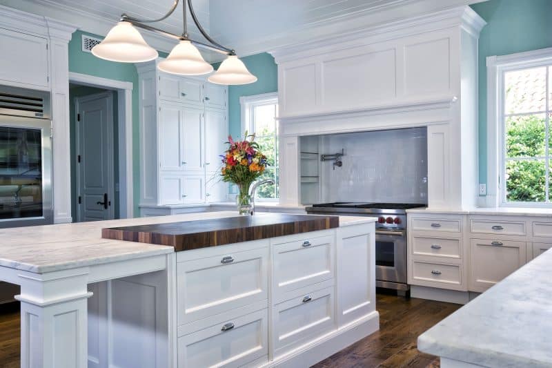 sky blue wall white with gray veining marble with part butcher block kitchen island top calling back hardwood floor and wall mounted pot filler faucet with white subway tiles backsplash