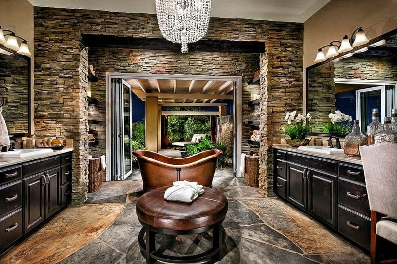 stone veneer walls and brown leather ottoman with round base and copper double slipper bathtub and beaded chandelier with large flagstone slab flooring