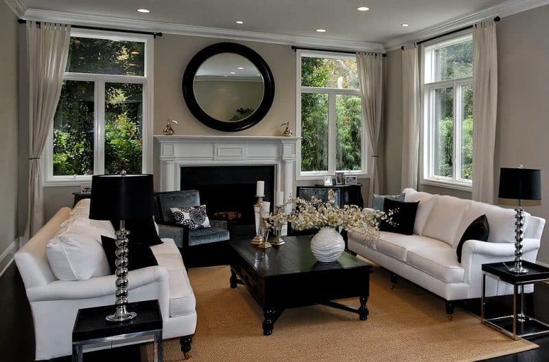 symmetrical living room layout with black framed round wall mirror as focal point and matching spiral chrome table lamp with black shade and black curtain rod