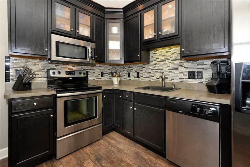 multi-toned gray mosaic tile backsplash with black corner cabinet with textured glass insert matching the illuminated upper cabinets and reclaimed hardwood flooring