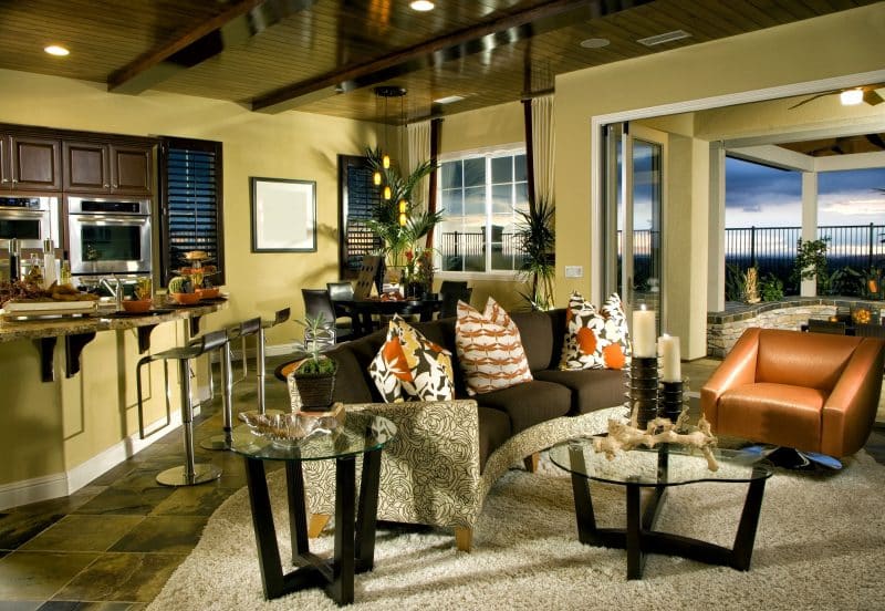 varnished dark wood beadboard ceiling panels with exposed laminated beams and slate stone tile flooring and brown curved sofa with orange accent chair