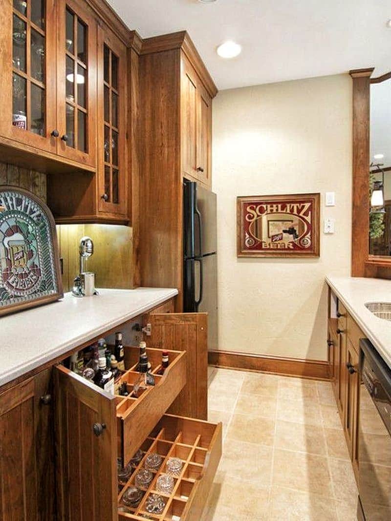 2 drawer-style wine cubbies and natural wood base cabinets with beadboard panels and curved white quartz countertop with sink and framed printed mirror on ecru wall and arched stained glass art with travertine tile flooring