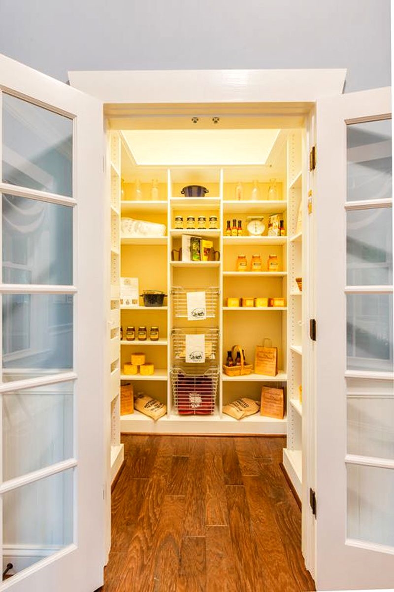 glass paneled white walk-in pantry doors and open box shelves with dandelion yellow rear wall and 3-tiered wire storage baskets with 4 white deep drawers and tray ceiling with cove lighting