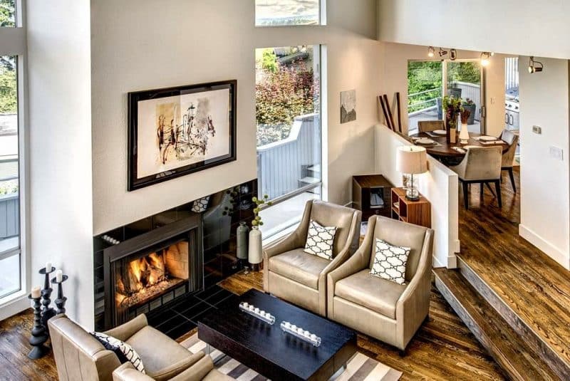 step-down living room with metallic leather chairs and black porcelain tiled fireplace surround and flush hearth with low back beige suede dining chairs and spotlight bars illuminating artwork with polished natural ash wood floors