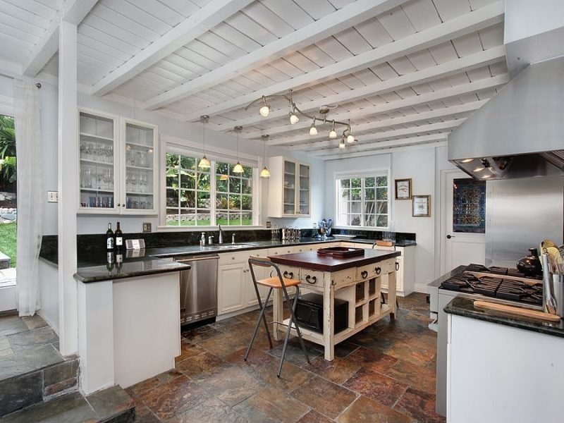 multicolored natural slate stone flooring with distressed free standing kitchen island and glass door floating cabinets and white side door with stained glass design and powder blue accent wall