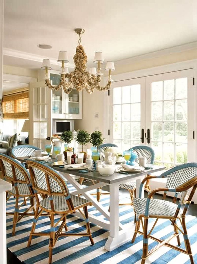 Parisian cafe-inspired bistro chairs and gray wooden tabletop with white cross stretcher and stripe flat-weave rug with oyster shell shade chandelier and in-swing French door to living room