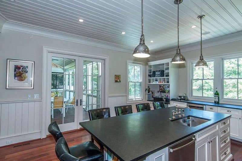 French door with decorative trims and soapstone island countertop with white recessed paneled base cabinets and black tufted leather bar stools with 3 satin nickel industrial pendant lights and wet bar with built-in wine cooler