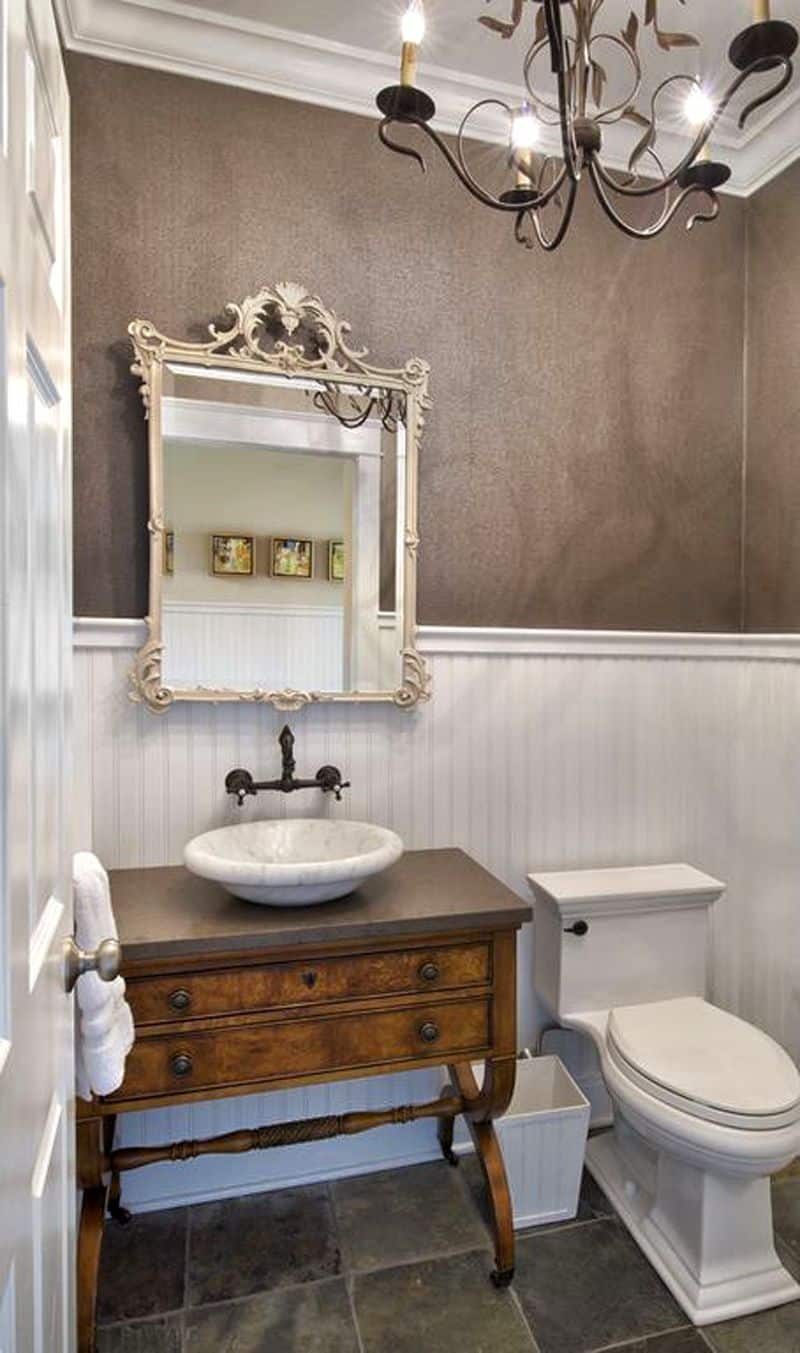 gray wall with white beadboard wainscoting and slate stone tile flooring with antique wood vanity with round marble vessel sink and candle-type wrought iron chandelier