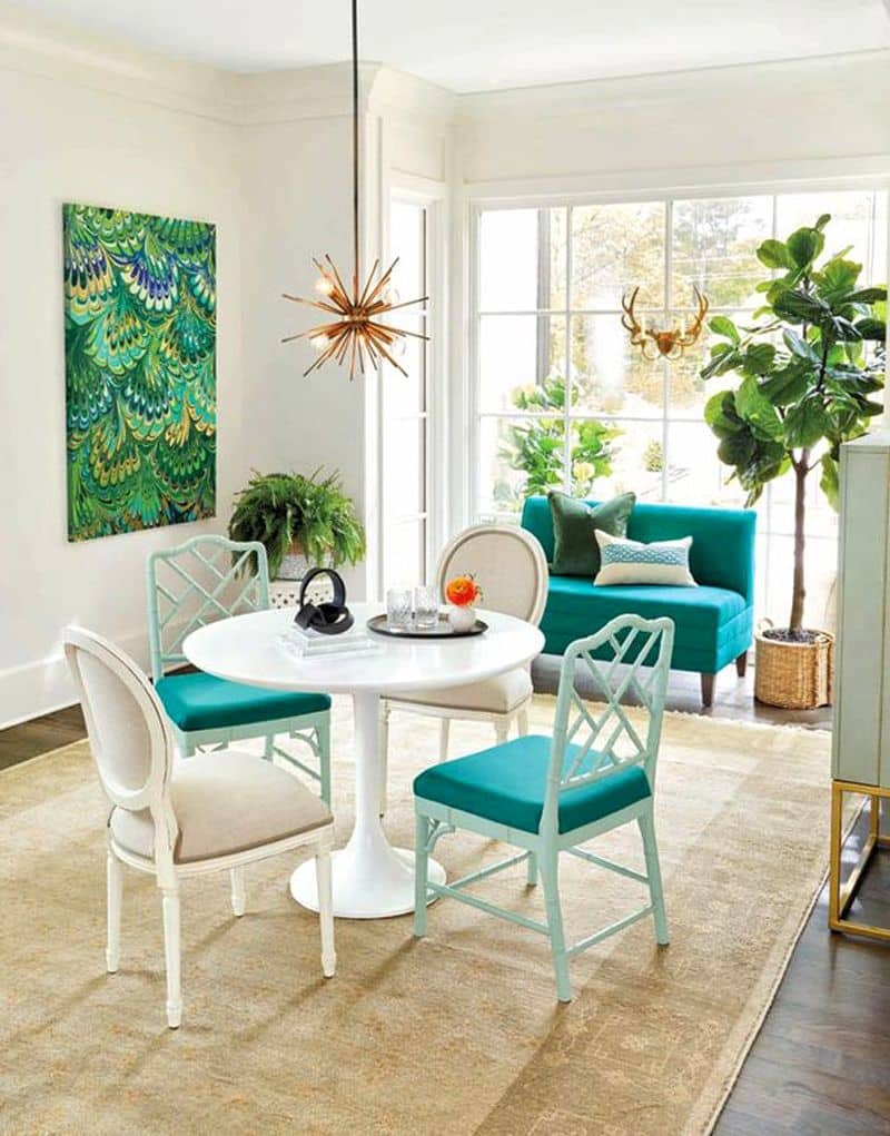 turquoise settee and dining chair cushions with white pedestal dining table and copper sputnik chandelier and linen white walls with large multi-toned green and blue peacock art