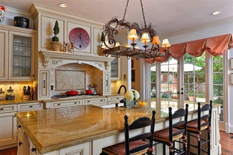 white French doors with matching sidelights and glazed cream seeded glass cabinets with black muntins and arched stove alcove with travertine mosaic stove backsplash and interior walls with salmon balloon valance