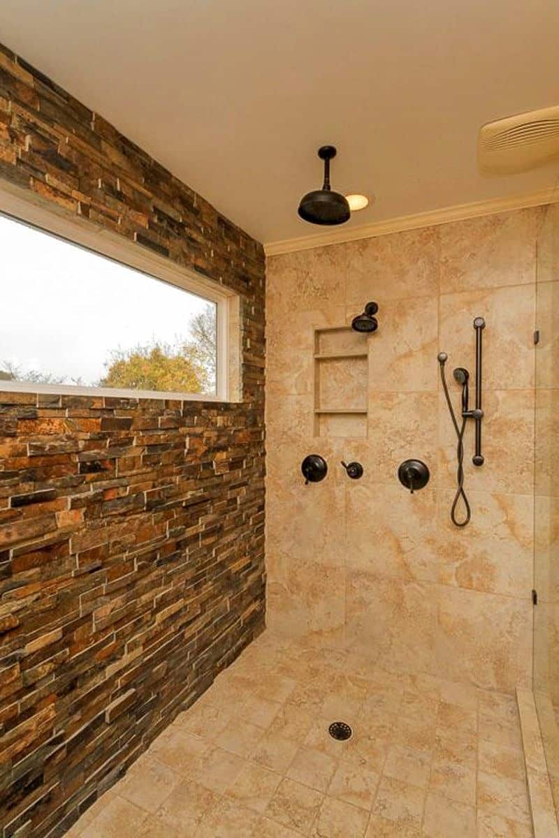 long rectangular picture window and stacked stone veneer accent wall with small wall niche with open shelves and walk-in shower enclosure with oil-rubbed bronze shower fixtures matching rain shower head with white ceiling with snap-in exhaust fan and recessed lighting